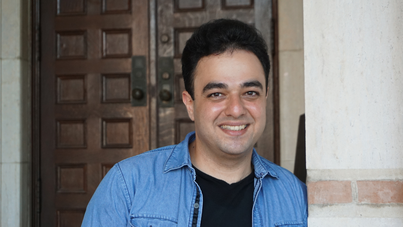 Rice CS PhD Student Mohammadamin Edrisi stands outside in front of a set of wood doors on the Rice University campus