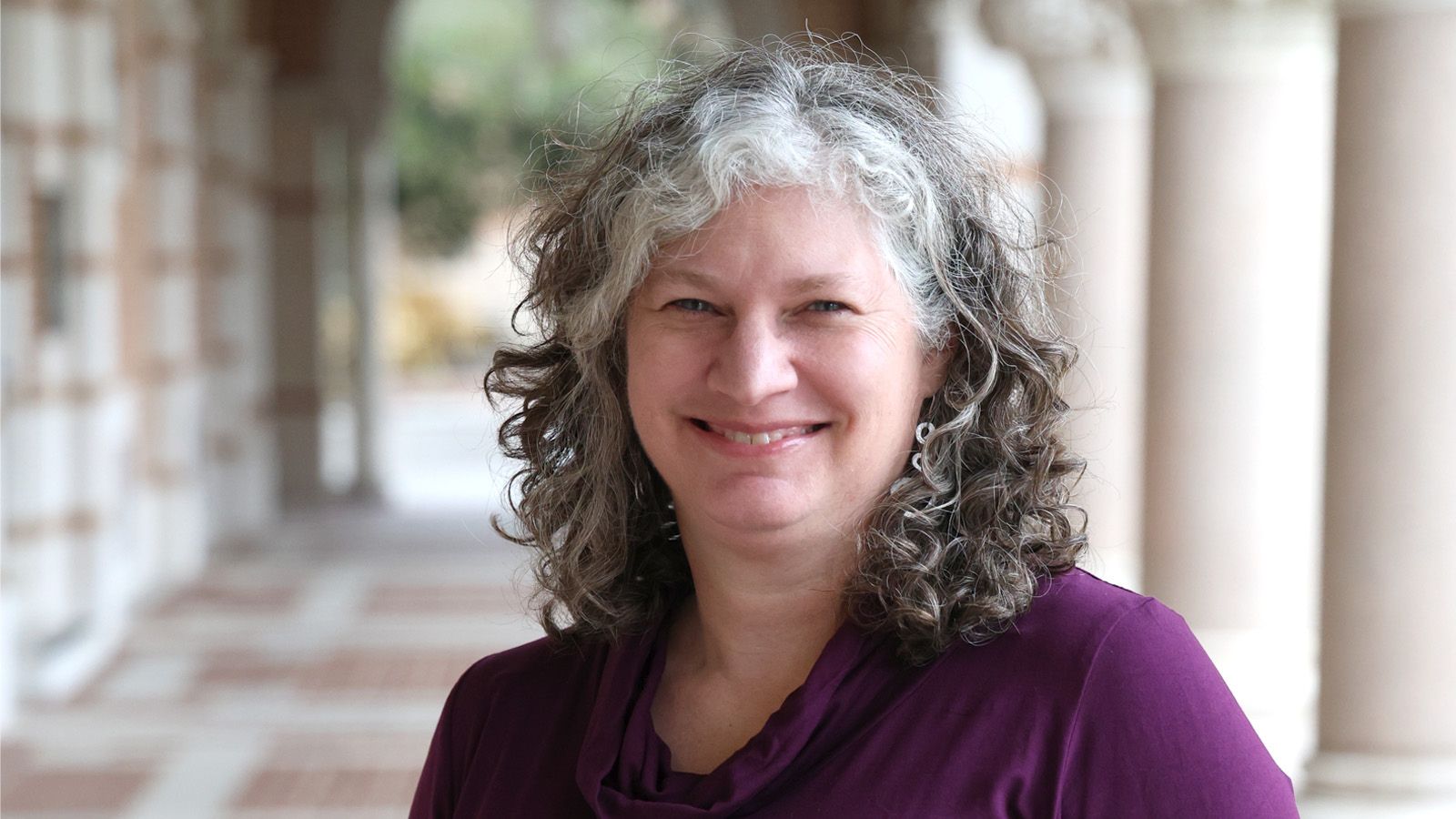 Woman in purple top stands in an outdoor stone hallway on Rice University's campus
