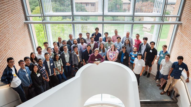 QuantIPS workshop participants stand on the building's stairwell in front of a wall of windows